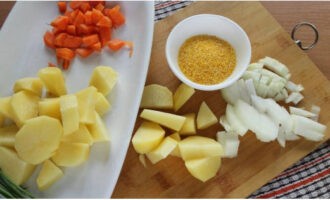 Peel the potatoes using a housekeeper and chop them coarsely. Chop the remaining carrots and onions into smaller pieces. Wash 2 tablespoons of corn grits well.