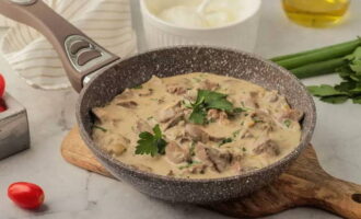 El hígado de pollo en crema agria con cebolla en una sartén está listo. Servir a la mesa, espolvoreado con hierbas picadas.