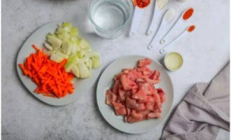 Lavamos y damos palmaditas a la carne, quitando las posibles gotas. Cortar en trozos arbitrarios del mismo tamaño.Retire la piel de las zanahorias con un pelador de verduras. Cortar el tubérculo en barras o rallarlo. Después de pelar la cebolla, cortarla en cubos.