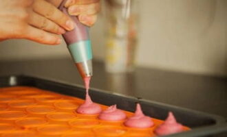 Placez la douille dans une poche à douille et remplissez-la de pâte. Disposez les biscuits sur un tapis en silicone. Tapotez la plaque à pâtisserie sur le bord de la table pour que la pâte se dépose et s'étale.