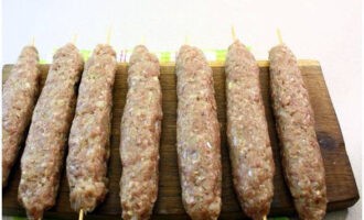 Wir befeuchten Holzspieße mit Wasser und machen aus dem vorbereiteten Hackfleisch jeweils eine Wurst darauf.