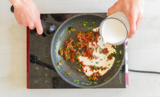 In einer Bratpfanne die Soße für die Paprika zubereiten. Knoblauch und Zwiebel schälen und fein hacken. Das Grün ebenfalls fein hacken. Zwiebel und Knoblauch in Pflanzenöl 2 Minuten anbraten. Dann Tomatenmark dazugeben und Sahne einfüllen.