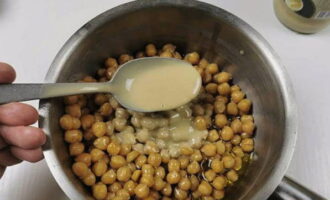 Scolare l'acqua dai ceci in una ciotola separata. Il decotto ci servirà più tardi. Aggiungere il tahini (pasta di sesamo) ai ceci. Se non avete la tahina potete tostare i semi di sesamo in una padella e tritarli in un frullatore con olio d'oliva.