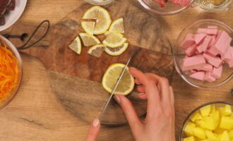 Como preparar uma clássica mistura de carnes com linguiça, picles e batatas? Depois de retirar a cebola da casca, lave-a e pique-a em cubos. Corte os tubérculos de batata descascados em cubos. Encha com água para evitar que escureça. Depois de descascar as cenouras, enxágue e rale bem. Pique a salsicha não muito grosseiramente. Lave o limão e corte em rodelas e depois corte em quartos.