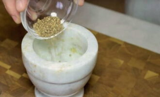 Next, let's prepare the spices. Add coriander seeds to a mortar and crush them using a pestle.