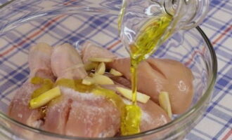 Add chopped garlic to the prepared chicken drumsticks, as well as salt (adjust to taste) and pour in olive oil.