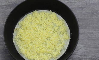 Grattugiamo il formaggio a pasta dura su una grattugia a fori medi e cospargiamo metà delle scaglie di formaggio sulla base del pane pita.