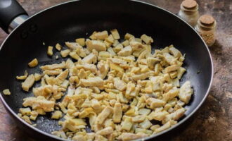 Droog de koekenpan op hoog vuur, giet er plantaardige olie in en verdeel het over het hele oppervlak. Bak eerst de plakjes champignons gedurende 2-3 minuten. Voeg hierna het eerder gehakte kippenvlees toe en bak alles nog 3-4 minuten samen, waarbij je de champignons en de kip af en toe roert met een spatel. De producten moeten lichtbruin zijn.