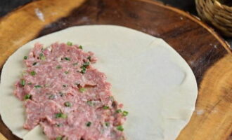 Ensuite, étalez les morceaux de pâte en galettes les plus fines possibles en vous éloignant légèrement du bord et étalez une couche de viande hachée.